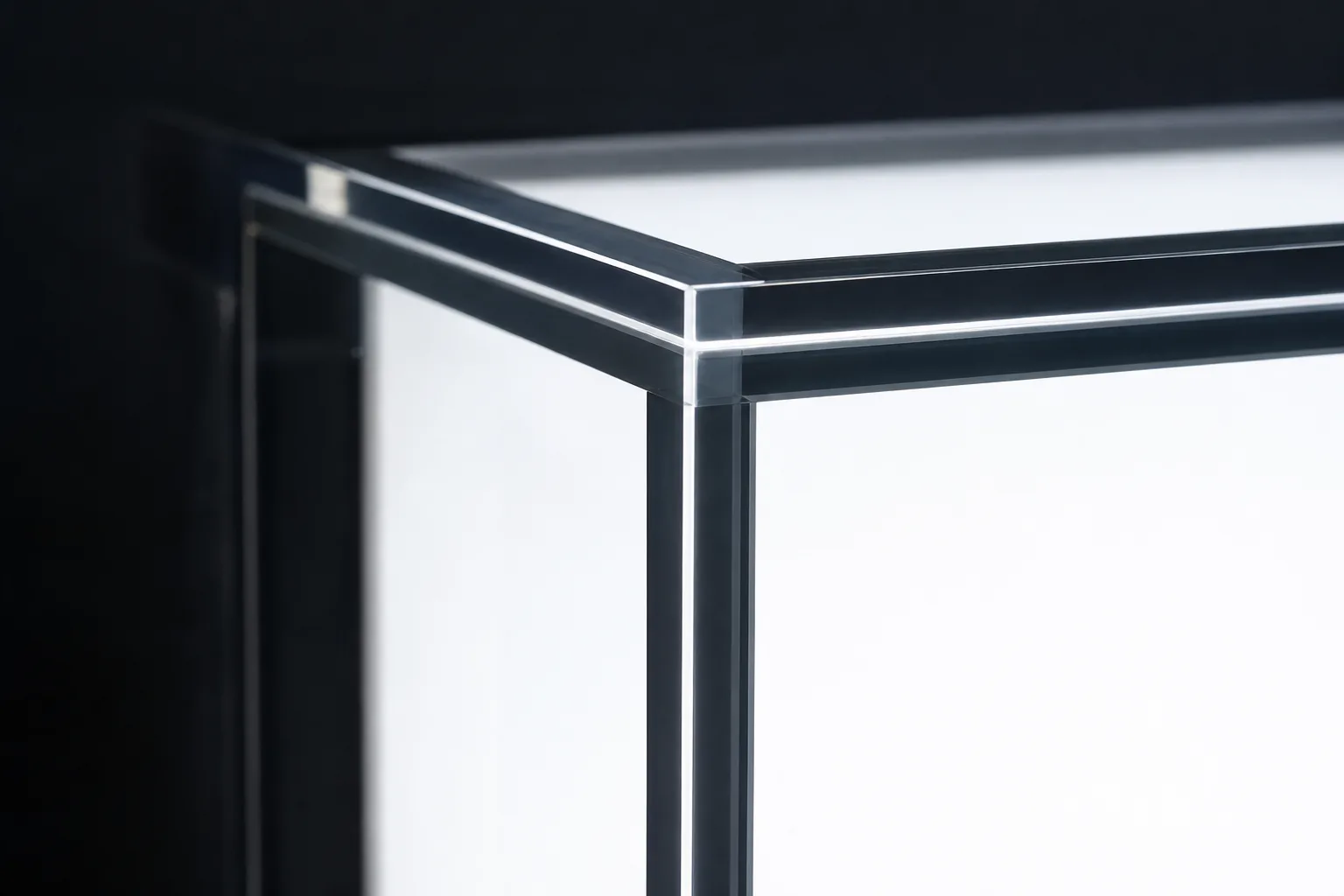 QC backlight inspection of a clear acrylic box seam — a bonded PMMA corner held against a light panel showing a uniform bubble-free solvent bond line
