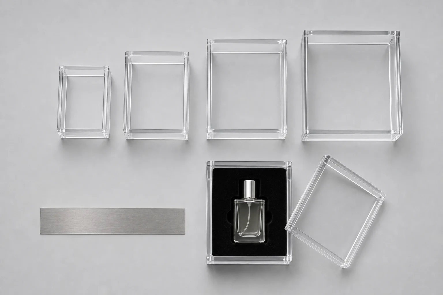 Overhead flat-lay of graduated clear acrylic gift box sizes with a steel ruler alongside, one open plexiglass box showing a velvet insert cavity sized around a small perfume bottle