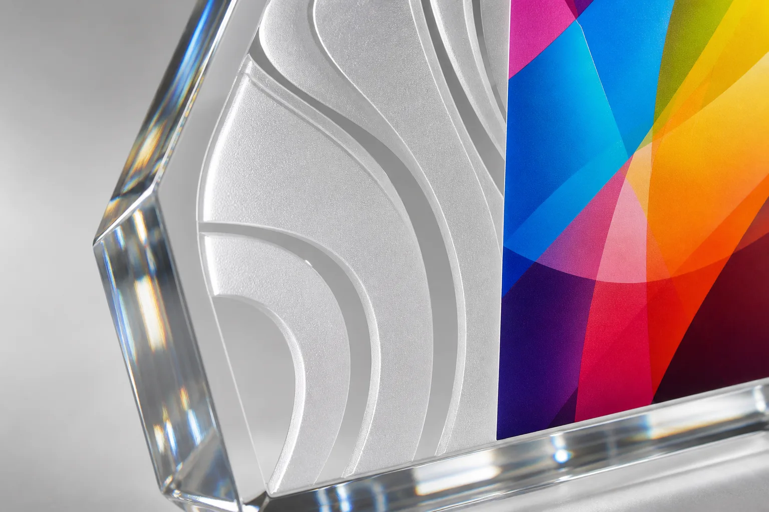 Close-up of a clear cast acrylic award with a laser-engraved frosted-white logo and a UV-printed full-color panel, beveled polished edges catching the light