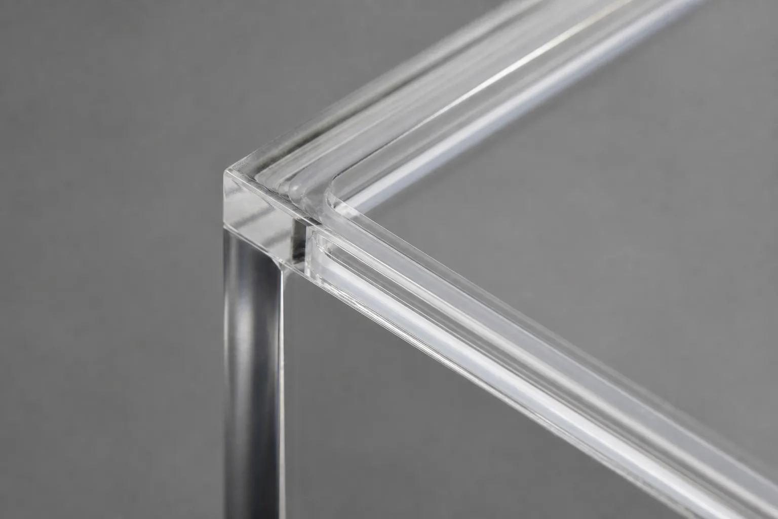 Corner of a solvent-bonded clear acrylic display box showing the fused PMMA seam and the machined recessed lip where the dust seal lid seats