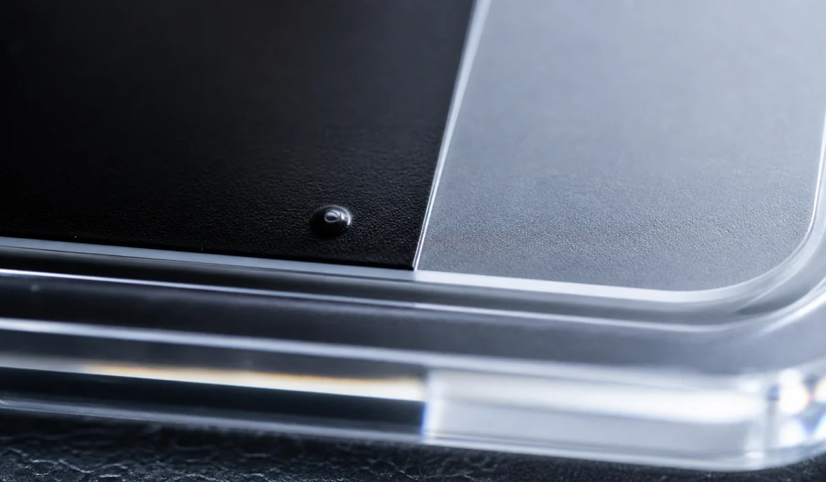 Extreme macro of a bottom-printed acrylic tray showing a tiny bubble defect under the ink layer beside a clean printed area