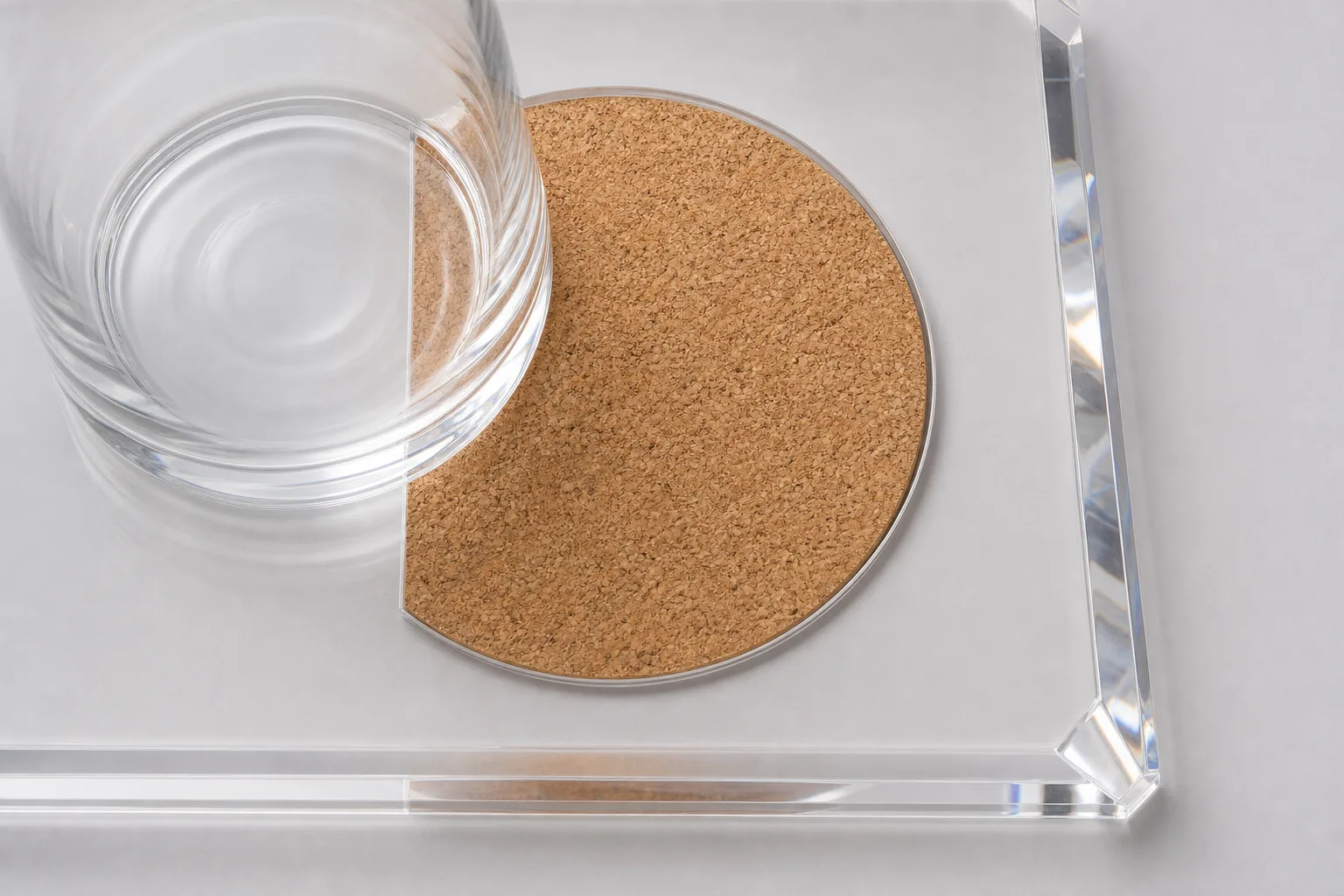 Clear acrylic serving tray with a recessed round cork insert seated flush in the bed, a single glass resting half on the cork pad and half on the surrounding acrylic