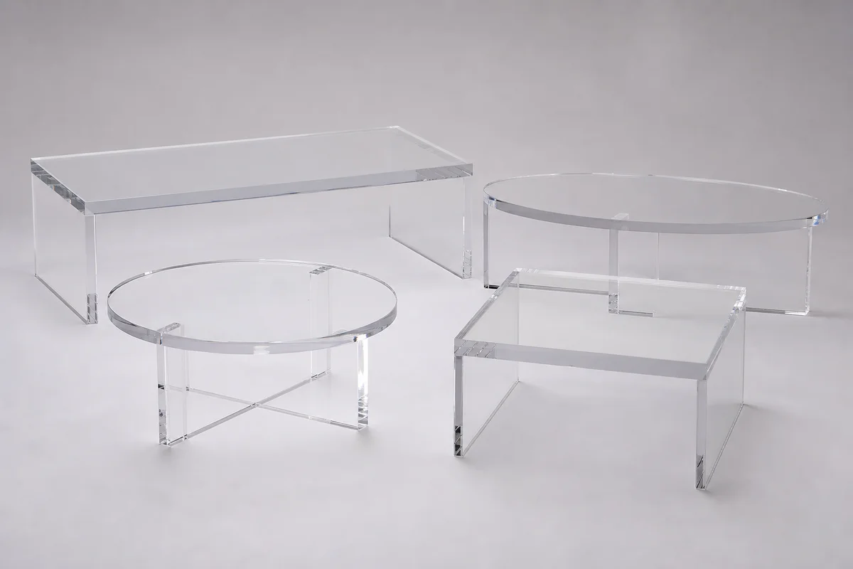 Editorial group shot of custom acrylic coffee tables in different shapes — rectangular, round, square, oval, and waterfall — arranged together on a neutral backdrop